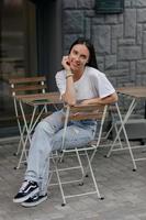 garota encantadora relaxada em camiseta de merda e jeans sentado no terraço de verão e posando para a câmera com um lindo sorriso foto