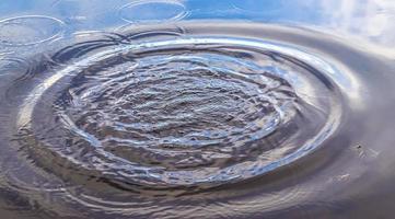 bela água em um lago com salpicos de água e ondulações na superfície com nuvens e reflexos do céu azul foto