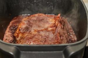 pedaço de carne é frito com cebola em molho de vinho em panela retangular sobre fogo no fogão a gás foto