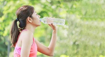 as mulheres asiáticas bebem água para matar a sede. depois de correr no parque. exercício saudável de conceito de férias foto