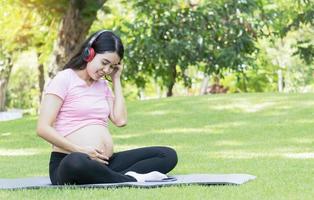 mulher grávida asiática sente-se e relaxe no parque ouvindo música. conceito de relaxamento de uma mulher grávida. foto