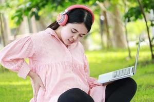 mulher grávida asiática sente-se e relaxe no parque ouvindo música. conceito de relaxamento de uma mulher grávida. foto