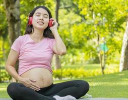 mulher grávida asiática sente-se e relaxe no parque ouvindo música. conceito de relaxamento de uma mulher grávida. foto