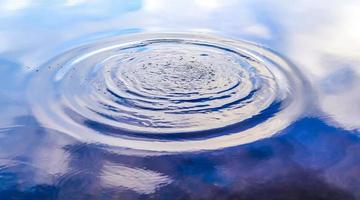 bela água em um lago com salpicos de água e ondulações na superfície com nuvens e reflexos do céu azul foto