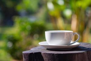 uma xícara de café branca na mesa de madeira com fundo natural no jardim foto