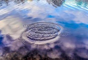 bela água em um lago com salpicos de água e ondulações na superfície com nuvens e reflexos do céu azul foto