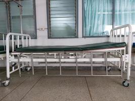 cama de hospital antiga com colchão verde, armação de aço branco, corrimãos prateados e rodas. foto