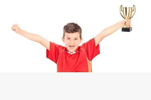 Júnior alegre segurando um troféu atrás de um painel