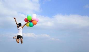 torcendo mulher pulando com balões coloridos para o céu azul foto
