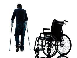 homem ferido com muletas andando longe da silhueta de cadeira de rodas foto