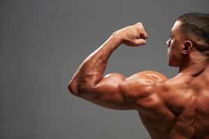fisiculturista masculina flexionando os bíceps, vista traseira com espaço de cópia foto