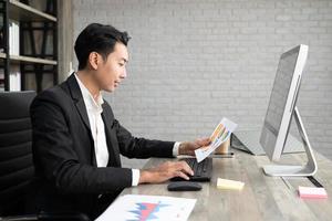 retrato de homem de negócios usando computador no local de trabalho em um escritório. homem de negócios positivo sorrindo olhando para o papel. foto