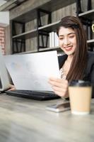 retrato de mulher de negócios bonita usando computador no local de trabalho em um escritório. senhora de negócios positiva sorrindo olhando no papel. foto