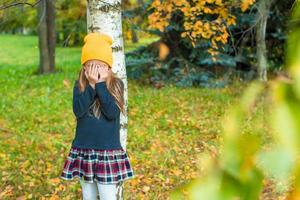 menina brincando de esconde-esconde perto de árvore no parque outono foto