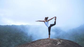 jovem exerce ioga nas montanhas. mulher asiática viajar natureza. viajar relaxar exercícios ioga tocar nevoeiro natural no pico da montanha. foto