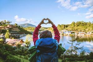 uma garota com uma mochila, desfrutando de uma viagem em uma montanha na zona rural. garota feliz com turismo relaxante, ela levantou a mão para fazer um formato de coração. foto