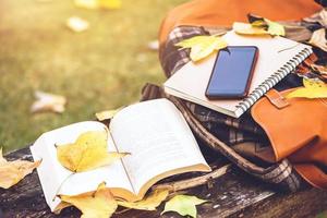 a mochila é colocada em uma mesa de madeira antiga com livros, cadernos, telefones e a natureza das folhas de bordo da vista superior. foto