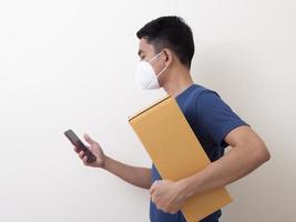 funcionário do serviço de entrega feliz com máscara facial médica carrega caixa de papelão na mão foto