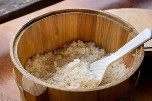 delicioso arroz simples cozido em uma grande tigela de madeira pronta para comer com colher de espátula de arroz branco na mesa do restaurante, close-up, estilo de vida. foto