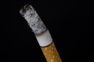 cigarro aceso com fumaça em fundo preto foto