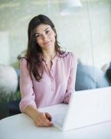 retrato de empresária jovem confiante usando o laptop na mesa de escritório foto