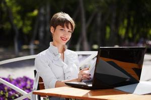jovem empresária com laptop em um café na calçada foto