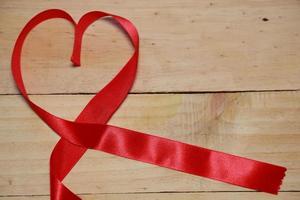 projeto consciência de fita em forma de coração vermelho em fundo de madeira envelhecido velho. conceito de dia dos namorados. espaço para texto. foto