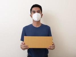 homem usando máscara cirúrgica com caixa de papelão em um fundo branco
