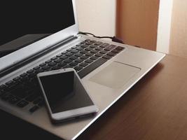 tela preta de smartphone em um teclado preto de computador portátil em um escritório de mesa com espaço de cópia e composição. negócio de escritório de conceito na internet e social foto