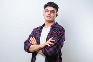 retrato de jovem asiático bonito vestindo camisa casual e óculos em pé com os braços cruzados e sorrindo para a câmera foto