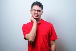 jovem asiático bonito vestindo camisa casual, tocando a boca com a mão com expressão dolorosa por causa de dor de dente ou doença dentária nos dentes foto