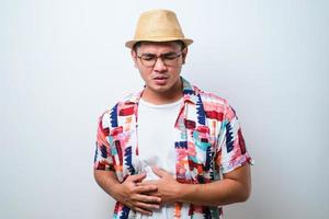 jovem asiático bonito vestindo camisa de praia casual e problemas de saúde de diarréia de chapéu de balde seguram sua barriga foto