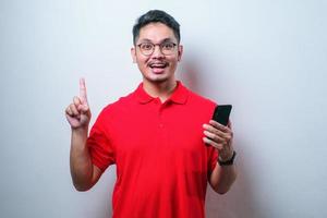 jovem asiático mostrando expressão feliz com o dedo apontando para cima enquanto segura o celular foto