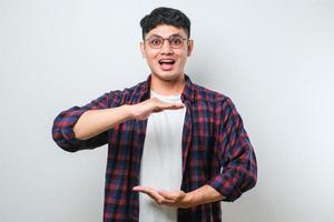 homem asiático bonito gesticulando com as mãos mostrando sinal de tamanho grande e grande, símbolo de medida. sorrindo olhando para a câmera. conceito de medição. foto