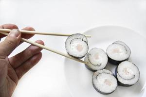 tomado com pauzinhos sushi com atum para comer. delicioso rolinho de peixe. rolo de sushi de arroz em uma esteira. foto