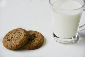 copo de vidro com leite em um fundo branco com biscoitos de aveia. almoço da tarde com biscoitos. biscoitos doces com leite. foto