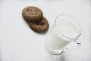 copo de vidro com leite em um fundo branco com biscoitos de aveia. almoço da tarde com biscoitos. biscoitos doces com leite. foto