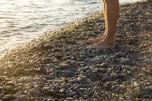 homem andando sozinho na praia de calhau ao pôr do sol foto