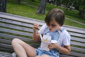 uma adolescente em uma caminhada em um dia de verão no parque almoça com macarrão wok foto