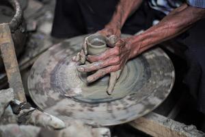 seletiva focada nas mãos sujas de pele enrugada do velho moldando o trabalho de barro na roda de fiar para fazer o jarro tradicional foto