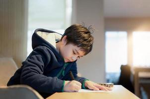 garoto da escola usando caneta preta desenhando ou escrevendo a carta no papel, menino fazendo lição de casa, criança com caneta escrevendo notas na folha de papel durante a lição. foto