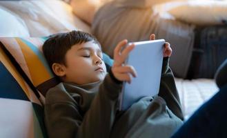 menino adormecendo enquanto assiste desenho animado no tablet, tentou garoto deitado na cama jogar online, criança dormindo enquanto lê e-book no tablet digital, menino de escola relaxando em casa foto