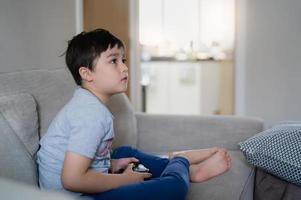 menino feliz jogando videogame on-line com amigos, criança fofa de tiro sincero sentado no sofá segurando o console do jogo. foto