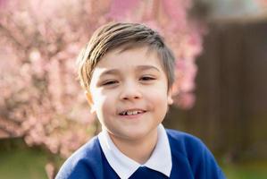 retrato menino feliz olhando para a câmera com rosto sorridente, garoto da escola em pé no jardim da frente esperando o ônibus escolar pela manhã foto