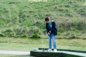 retrato criança ativa jogando mini golfe no parque, menino bonitinho fazendo atividade ao ar livre jogando golfe louco no campo de primavera, crianças se divertindo lá fora com a família em dia ensolarado de verão foto