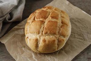 pão boule caseiro em papel pardo, mesa de madeira rústica foto