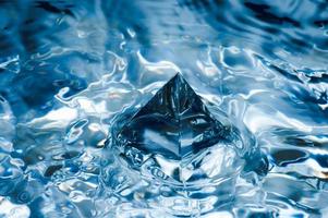 abstrato azul com salpicos de água e um objeto geométrico. pirâmide na água. foto