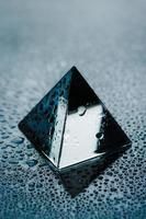 objeto geométrico brilhante com gotas de água. pirâmide transparente molhada close-up vista. foto