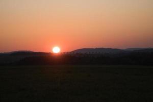 romântico pôr do sol atrás de uma colina em frente a um prado. foto