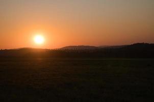 romântico pôr do sol atrás de uma colina em frente a um prado. foto